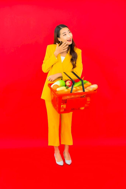 Portrait beautiful young asian woman with grocery basket from supermarket on red background - 写真・画像