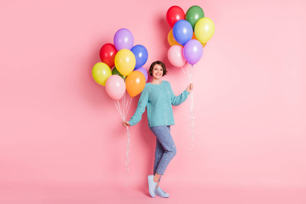 Full size photo of optimistic curly brunette hairdo lady hold balloons wear blue sweater jeans sneakers isolated on pink color background - Foto, Bild