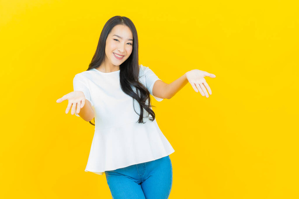 Retrato hermosa joven mujer asiática sonrisa con acción sobre fondo de color amarillo - Foto, Imagen
