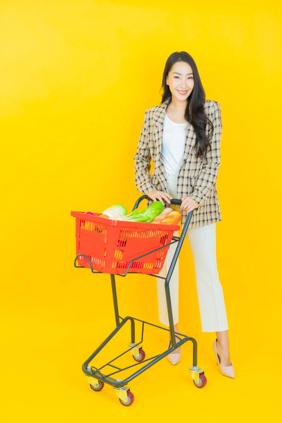 Portret mooie jonge aziatische vrouw glimlach met kruidenier mand van supermarkt op kleur achtergrond - Foto, afbeelding