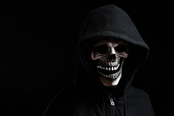 Die Totenkopfmaske mit Kapuzenshirt im dunklen Hintergrund. - Foto, Bild