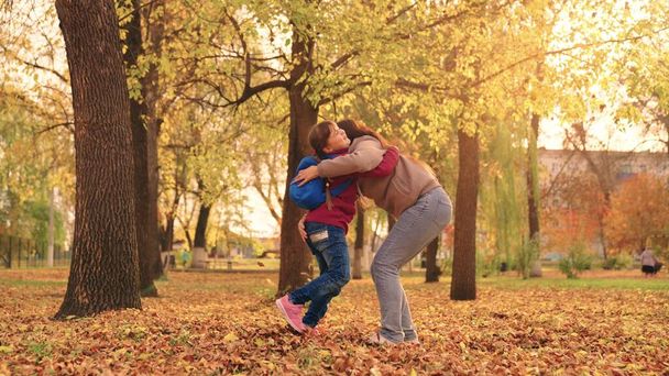 äiti ja pieni lapsi syksyllä puistossa heittää kuivia lehtiä, onnellinen perhe, elää hauskaa äidin kanssa, iloinen lapsi leikkii lehtien ja vanhempien käsien kanssa heittämällä lehtiä syksyllä, vanhempien hoito tytöstä, luontokävely. - Valokuva, kuva