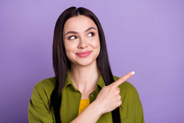 Photo of adorable pretty young woman wear khaki outfit pointing finger looking empty space smiling isolated violet color background - Foto, Imagem