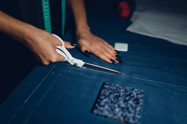 de kleermaker knipt de stof met een schaar. productie van kleding met de hand volgens individuele normen. de mode-industrie. de modeontwerper werkt thuis - Foto, afbeelding