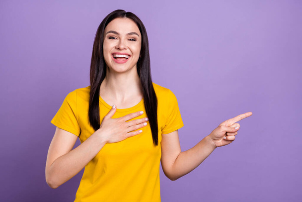 Фото блискучої смішної молодої жінки в жовтому вбранні, вказуючи пальцем порожній простір рук грудей посміхаючись ізольований фіолетовий кольоровий фон
 - Фото, зображення
