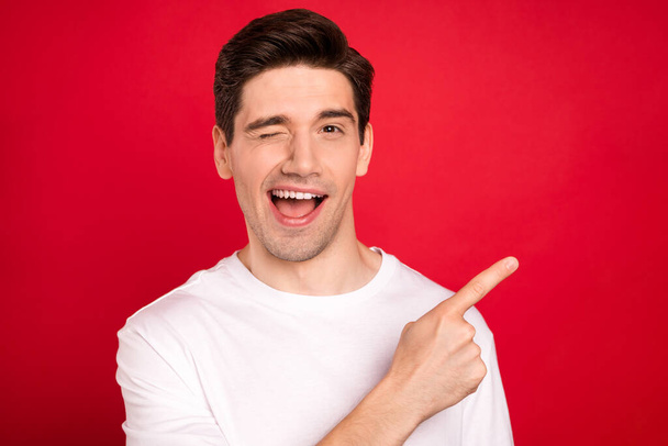Photo portrait brunet wearing casual t-shirt blinking pointing finger copyspace isolated bright red color background - Φωτογραφία, εικόνα