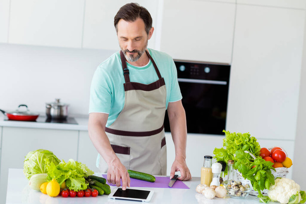 Photo of masculine aged man cook salad look video tablet wear apron blue t-shirt home kitchen indoors - Fotoğraf, Görsel