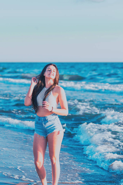 Nuori nainen leikkii meressä kesällä. Nainen nauttii merivedessä. Iloinen nuori nainen hauskaa rannalla. Hän on rentoutunut merivedessä ja nauttii lomasta. - Valokuva, kuva