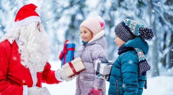 Santa Claus giving any present boxes for children in the snowy park - Foto, Imagen