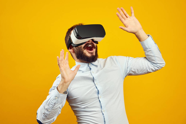 Fröhlicher junger bärtiger Mann mit Virtual-Reality-Helm, der die Luft berührt - Foto, Bild