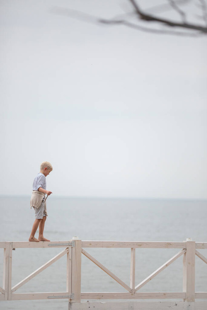 the boy walks along the beach on a white fence and balances - Photo, image