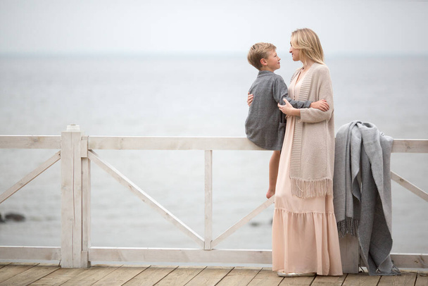 Mom in a pink dress with her little son standing on the seashore - Photo, image