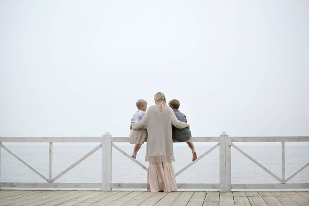 mother in a long dress hugging her sons, standing near a white wooden fence. Family boat trip - Foto, afbeelding