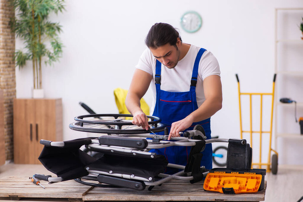 Young male repairer repairing wheel-chair indoors - Foto, afbeelding