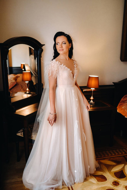 Retrato de la novia en un vestido de novia en el interior de la casa cerca del espejo. - Foto, Imagen