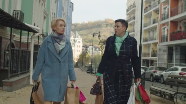 Aikuiset naiset paperipussit kävely katu kaupunkikuva taustalla - Materiaali, video