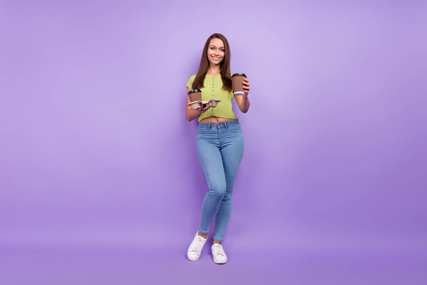 Πλήρες μήκος του σώματος άποψη του μεγέθους ελκυστικό χαρούμενο κορίτσι κρατώντας δύο φλιτζάνια latte δίνοντάς σας απομονωμένο σε μωβ βιολετί φόντο χρώμα - Φωτογραφία, εικόνα