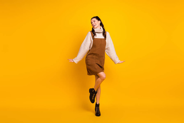 Вид в полный рост на привлекательную жизнерадостную девочку-карусель, прыгающую весело, изолированную на ярко-желтом фоне - Фото, изображение