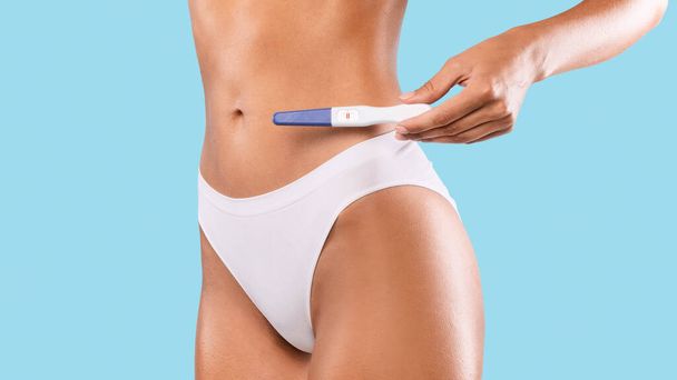 Woman holding positive pregnancy test wearing white underwear - Fotoğraf, Görsel