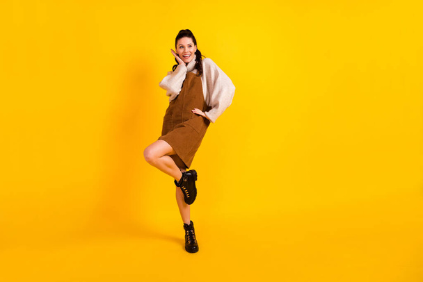 Full length photo of carefree charming woman wear brown dress dancing hand arm cheek cheekbone isolated yellow color background - Photo, Image