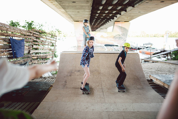 Eine Gruppe von Teenagern reitet auf einer Rampe im Skatepark. Die Kleinen vergnügen sich gemeinsam auf dem städtischen Sportgelände beim Skateboarden. Sportverein für Kinder. Spielerisches Geschick. Skateboarding Club für Kinder - Foto, Bild