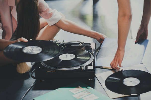 Fiatal nők ülnek a földön, és felfedezik a bakelit lemezeket, és retro lejátszóra teszik őket.. - Fotó, kép