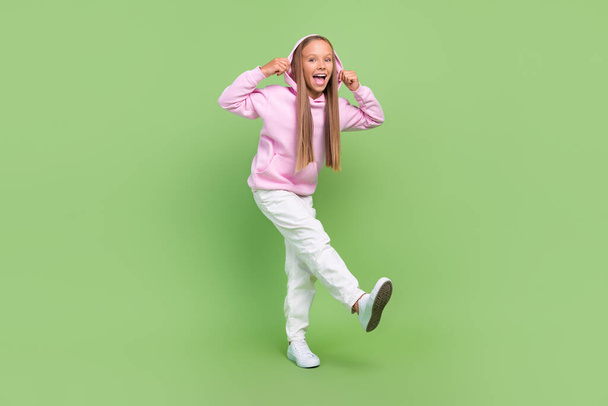 Full size photo of cheerful excited nice positive young small girl wear hoodie street style isolated on green color background - Photo, Image
