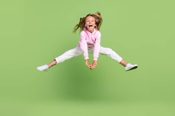 Full length photo of funky small blond girl jump wear sweatshirt trousers sneakers isolated on green background - 写真・画像