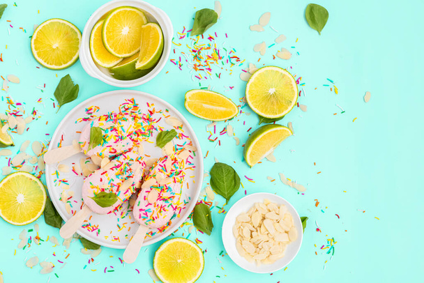 Bright and colorful flat lay of pink strawberry Popsicle ice cream with sliced lime and mint on blue background. Healthy summer food concept. Top view of popsicle with sprinkles, overhead - Photo, Image