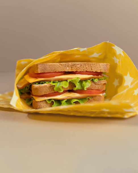 Un sándwich tradicional hecho de rebanadas de pan tostado, queso, jamón, ensalada fresca envuelta en papel orgánico de cera de abeja reutilizable. Celebrando el Día Nacional del Sandwich. - Foto, Imagen