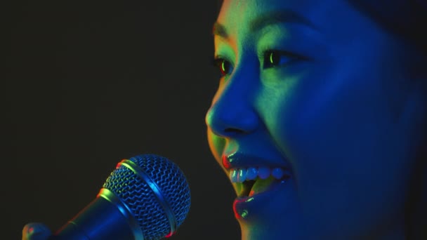 Jovem feliz mulher asiática cantora cantando em microfone em luzes de néon brilhantes, vida noturna e conceito de karaoke, retrato de perfil - Filmagem, Vídeo