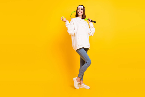 Photo of active lady hold racket ball look empty space wear headband hoodie jeans shoes isolated yellow color background - Foto, Imagem