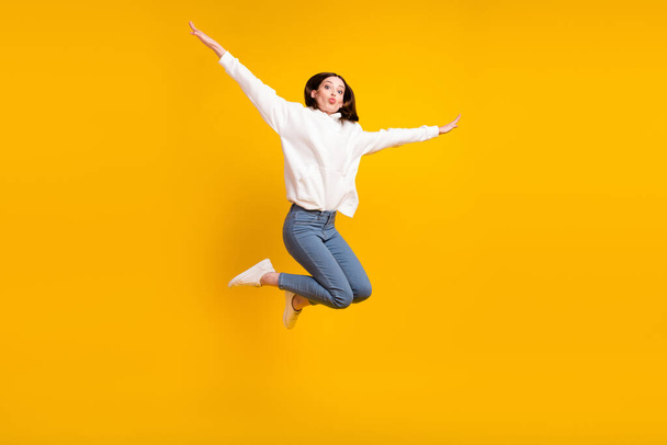 Photo of romantic lady jump plane flight blow air kiss wear white hoodie jeans shoes isolated yellow color background - 写真・画像