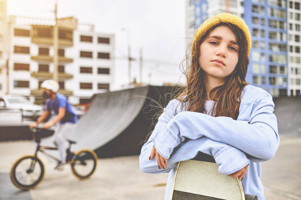 Dziewczyna bawiąca się jazdy na deskorolkach w skate parku, Portret uśmiechniętej młodej skateboardzistki trzymającej jej deskorolkę. Koncepcja działalności rekreacyjnej. - Zdjęcie, obraz