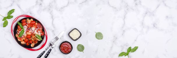 Ньокки с помидорами, красным соусом, сыром и листьями базилика на мраморном фоне. Выборочный фокус. Вид сверху.  - Фото, изображение