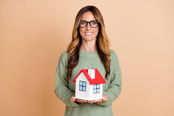 Photo portrait woman wearing glasses smiling keeping little house isolated pastel beige color background - Φωτογραφία, εικόνα