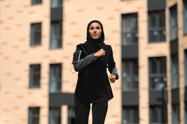 Urbaani urheilu. Muotokuva motivoitunut muslimi nainen vaatimaton urheiluvaatteet käynnissä ulkona - Valokuva, kuva