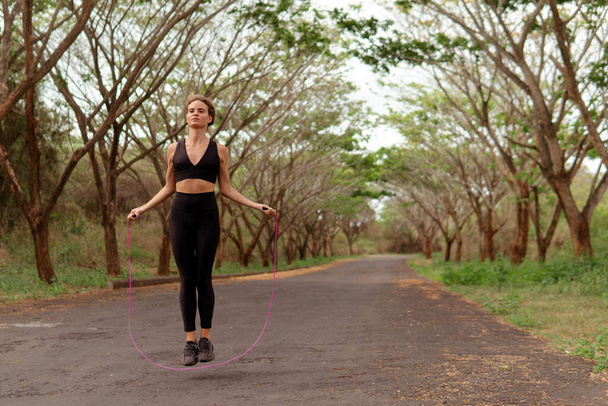 Woman in black sportwear jumping rope - Photo, Image