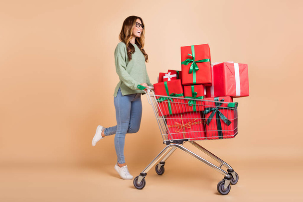 Full length body size view of pretty cheerful woman carrying giftboxes holiday isolated over beige pastel color background - 写真・画像