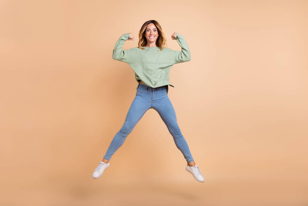 Full length body size view of lovely cheerful woman jumping showing stength isolated over beige pastel color background - Fotó, kép