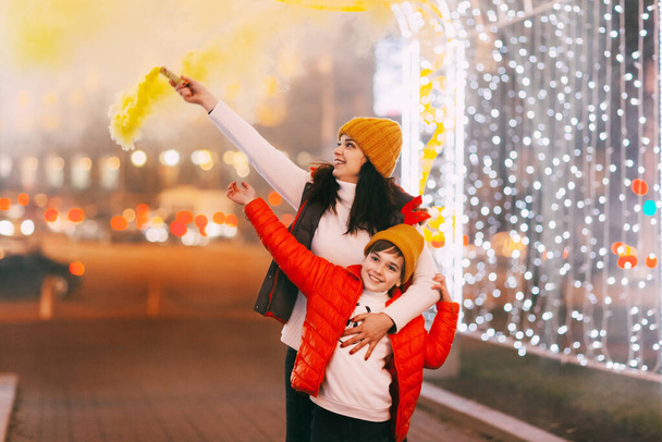 Mamá y su hijo sostienen bombas de humo de colores en sus manos durante la celebración de Navidad o Año Nuevo - Foto, imagen