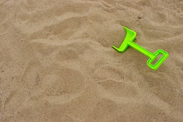bright green plastic toy shovel on background of brown sand with copy space  - Photo, Image