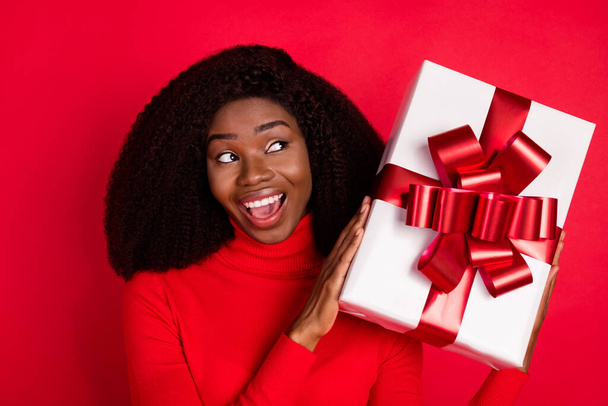 Photo of young excited black woman happy positive smile hold gift box birthday celebration isolated over red color background - Foto, immagini
