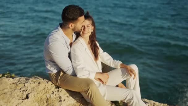 Χαμογελαστό ζευγάρι που μιλάει σε βράχο ενάντια στη θάλασσα - Πλάνα, βίντεο