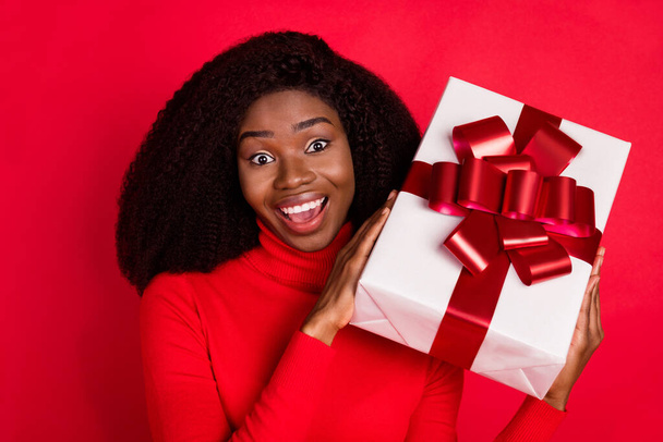 Photo of young excited black woman happy positive smile hold present box birthday party isolated over red color background - Fotografie, Obrázek