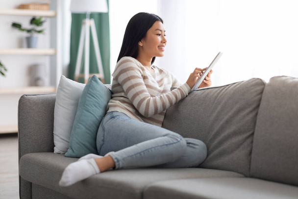 Portrait Of Beautiful Smiling Asian Woman Resting On Couch With Digital Tablet - Фото, изображение