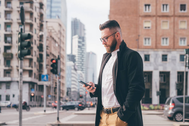 Young serious caucasian businessman outdoor walking using smartphone browsing internet 5g technology, watching video streaming or playing games - Foto, Imagen