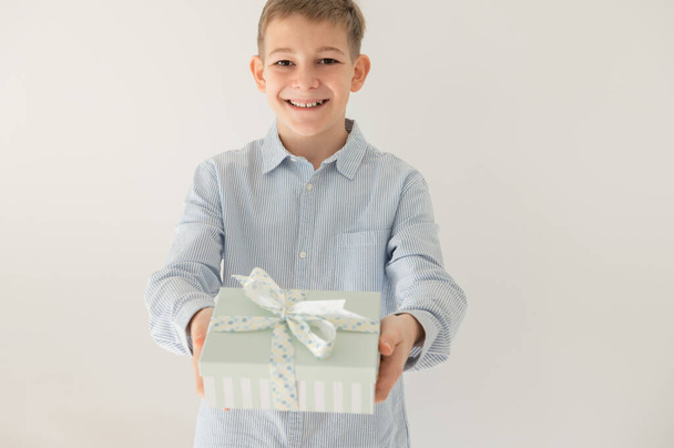 Cute smiling teenage boy giving beautiful gift box as birthday or christmas surprise - Photo, Image