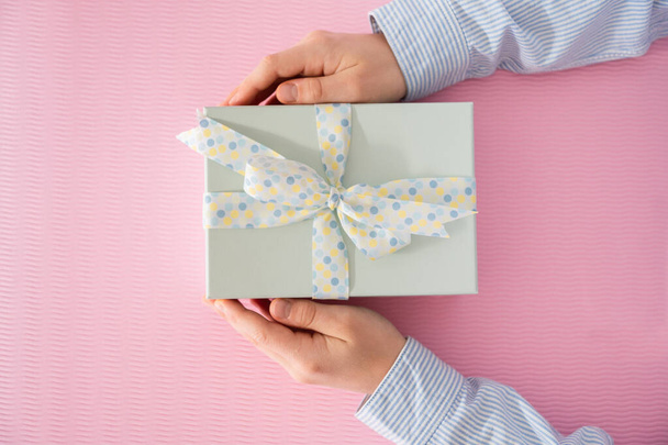 Flat lay photo of beautiful wrapped present box and hands holding gift box on pink background - Foto, afbeelding