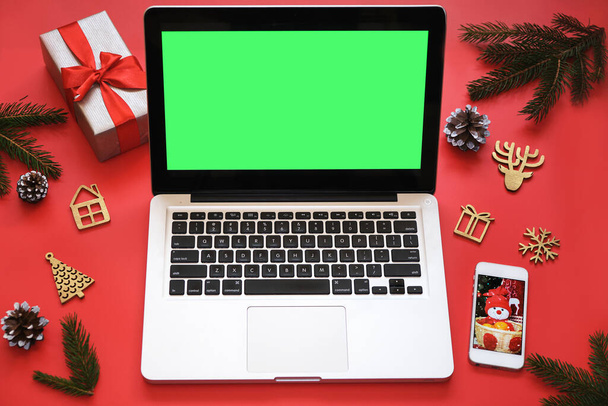Laptop with green screen, mobile phone and Christmas decorations on red background.Concept: selection gifts, online shopping, Christmas sales, seasonal advertising.Mockup postcard, holiday invitation. - Foto, Imagem
